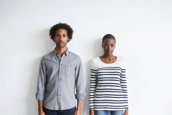 Couple, serious and portrait by white wall in fashion with confidence, casual style and model aesthetic. Black woman, and face of man with trendy apparel, edgy clothes and pride with calm expression.