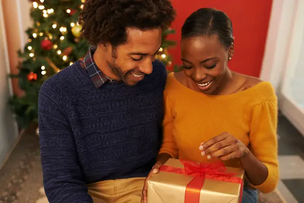 Christmas, present and black couple giving a box or opening surprise on festive holiday or vacation with happiness. Excited, woman and man offer a gift in home with love and kindness in marriage.