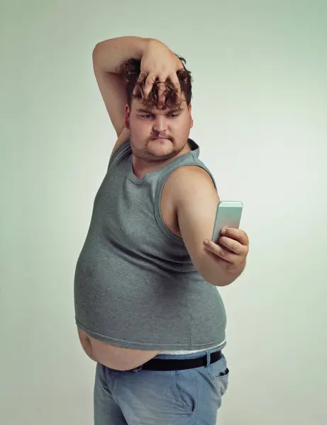 スタジオのセルフィー 携帯電話 プラスサイズの男性は カジュアルでトレンディで 胃でクールな服を着ています グレーの背景で隔離された写真を持つ男性と電話 深刻で面白い — ストック写真