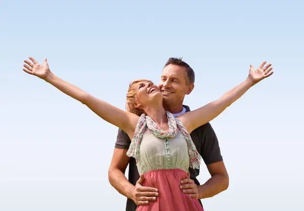Couple, hug and smile with love outdoors for honeymoon vacation, together and arms up for freedom. Man, woman and relationship with care for romance, marriage and support with trust for happiness.