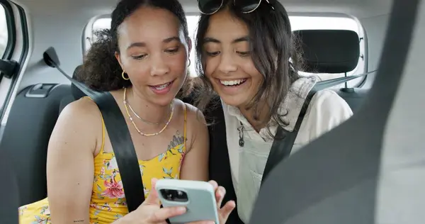 Happy friends, phone and car for road trip information, location search and social media. Young women reading on mobile app and talking of travel, holiday and transportation service with funny chat.