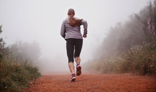 Woman, rear view and running in woods with fitness for exercise, morning routine and workout with fog and legs. Athlete, person and cardio with sportswear on outdoor trail and forest for wellness.