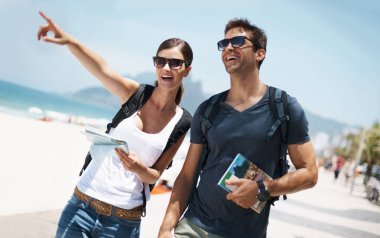 Couple, holiday and pointing with map at beach as tourist in summer, trip and smile for adventure in Brazil. Directions, relationship and bonding on vacation in seaside for travel, break and happy. clipart