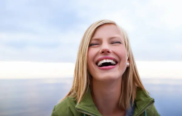 Woman, excited and happy at the beach for holiday, vacation and travel in winter. Face of a young person in the USA laughing and smile by an ocean, sea or lake with cloudy sky for outdoor adventure.