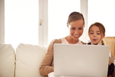 Laptop, sınıf ya da birlikte ders çalışmak için anne ve kızıyla birlikte oturma odasındaki kanepede oturarak para kazanmak. Bilgisayar, kadın ebeveyn ve kız çocuğunun evde büyümesi için uzaktan ders ya da ev ödevi.