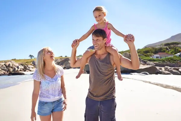 Happy family, beach and piggyback with child for fun summer, holiday or outdoor weekend in nature. Mother, father and little girl with ride on shoulders in freedom, bonding or love by the ocean coast.