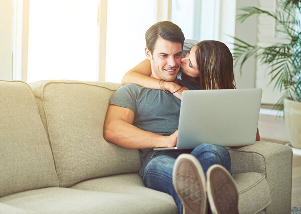 Laptop, kiss and woman hugging man on sofa networking on social media, website or internet. Happy, love and female person embracing husband reading online blog with computer in living room at home