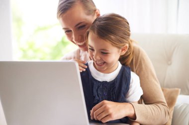 Dizüstü bilgisayar, eğitim ya da birlikte çalışmak için evdeki oturma odasındaki kanepede anne ve kızıyla gülümsemek. Okul, ev ödevi ya da internetten kadın ebeveyn ve kız çocuğunun evde büyümesi.