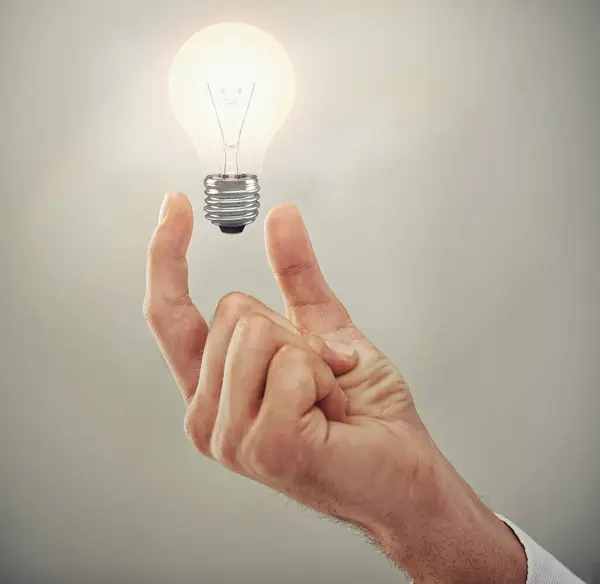 Hand, light bulb glow and ideas for business growth and development isolated on grey background. Person with insights, corporate innovation and knowledge for enlightenment and inspiration in studio.