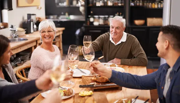 Cheers, wine and family at dinner in dining room for party, celebration or event at modern home. Smile, bonding and group of people enjoying meal, supper or lunch together with champagne at house