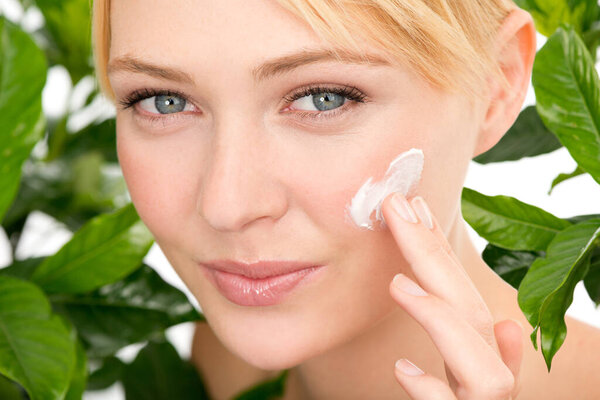 Portrait, skincare and woman with cream by leaves isolated on a studio background for health or hydration. Face, cosmetics and natural model with lotion for organic facial moisturizer or dermatology.