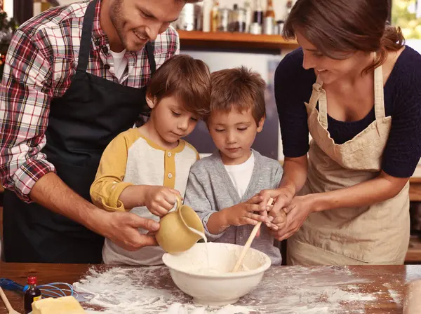 キッチンでベイキング 幸せな男の子は 家庭で両親と結びついています 小麦粉で調理する父 母または子供 食べ物と兄弟は テーブルにボウルにミルクを注ぐ — ストック写真