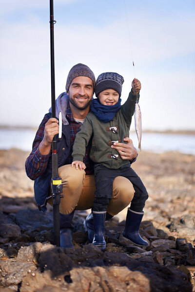 Portrait, son and smile with father, fish and happiness for achievement on break. Family, water and ocean with rocks, adventure and vacation on bonding fishing trip for childhood memories and success.
