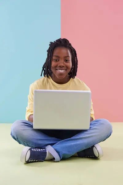 stock image Teenager, portrait and laptop in studio for online education, e learning and creativity on the floor. Kid, student or African boy with computer for school in pastel color or blue and pink background.