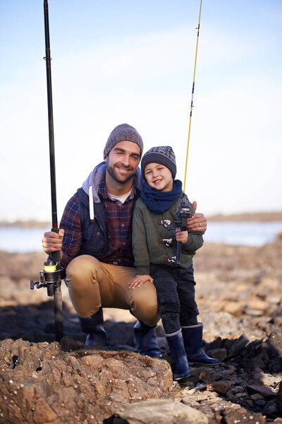Portrait, dad and son with nature, smile and happiness for bonding on break. Child, water and ocean with rocks, adventure and vacation on fishing trip with childhood memories and parent fun at sea.