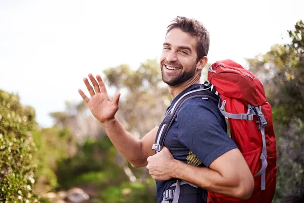 Man, hike and happy with wave for adventure with backpack for fitness, workout and hobby in Canada. Portrait, smile and outdoor activity in nature for healthy mind in woods on summer holiday