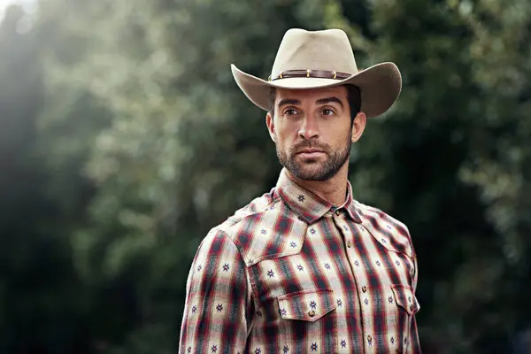 Man, style and outdoor cowboy fashion, western culture and countryside ranch in Texas. Male person, hat and flannel clothes for farmer aesthetic, nature and plaid trend by trees or outside bush.