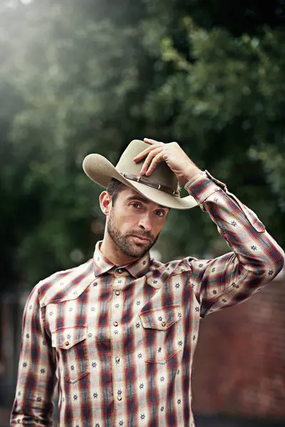 Man, portrait and outdoor cowboy style, western culture and countryside ranch in Texas. Male person, hat and flannel fashion for farmer aesthetic, nature and plaid trend by trees or outside bush.