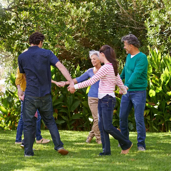 Happy family, holding hands and dance together outdoor or play game in summer in a circle with grandparents. Ring a rosy, smile and children in garden on holiday, vacation and bonding with parents.