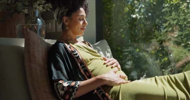 赤ちゃんのための興奮 幸せな腹への愛で自宅の黒人女性 妊娠中と窓 未来のお母さん お腹とソファーを持って 産婦人ケアのアイデアに疑問を抱く — ストック動画