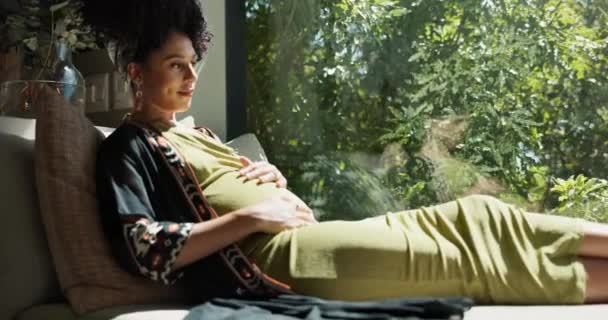 赤ちゃんのための興奮 幸せな腹への愛で自宅の黒人女性 妊娠中と窓 将来の母親は お腹とソファーを保持し お母さんケアのための疑問やアイデア — ストック動画