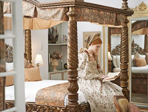 Woman, queen and book with reading for renaissance, royalty aesthetic and confidence on palace bed. Monarch, wealthy person and elegant dress for cosplay, regal and medieval knowledge in the castle.