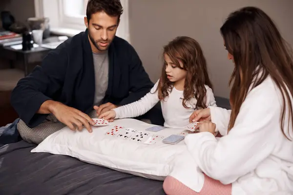 Parents, girl and fun with playing cards for game for bonding, learning and relax with strategy in bedroom. Father, mother and daughter with deal, maths and teaching with connection in family house.