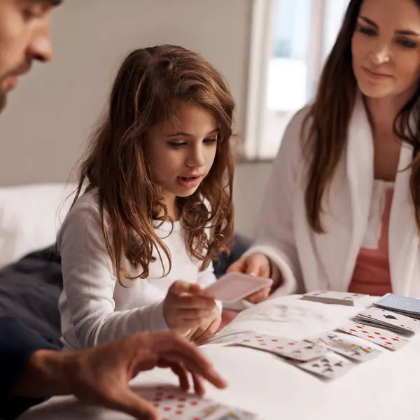 Parents, girl and fun of playing cards in home for bonding, learning and relax with strategy in bedroom. Father, mother and daughter with games, maths and teaching with connection in family house.