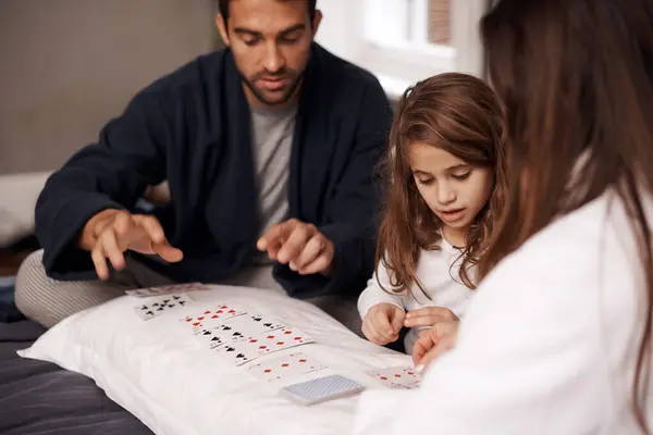 Mom, father and girl with playing cards for competition with bonding, learning and relax with strategy in bedroom. Dad, mother and daughter with deal, deck and child on bed with game in family house.