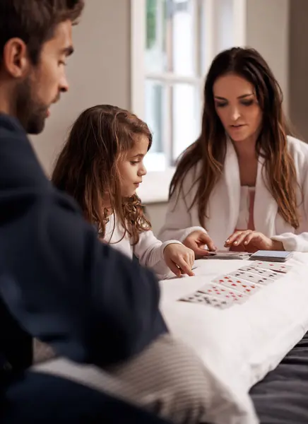 Mom, dad and girl with playing cards in home with bonding, learning and relax with strategy in bedroom. Father, mother and daughter with deal, game and teaching on bed with connection in family house.