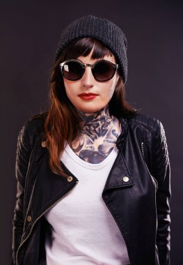 Güneş gözlükleri, dövme ve stüdyoda siyah arka planda ceketli bir kadın. Esmer, deri ve havalı kadın punk modeli. Benzersiz sanat, moda ya da yaratıcı ifade için mürekkebi var..