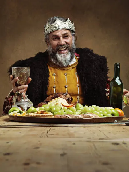 King, feast and happy in table with wine glass as lord on dining hall for tradition, culture and meal in palace. Portrait, monarch and leader with eating buffet or supper in royal party with crown.