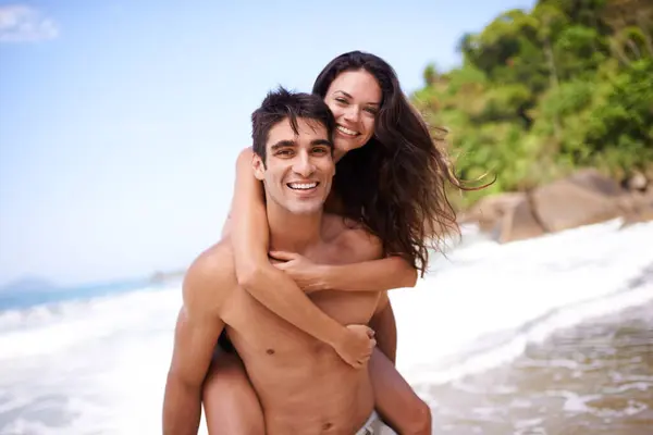 Piggyback, love and portrait of couple at beach on vacation, adventure or holiday for romantic travel. Happy, smile and young man and woman on date by ocean for tropical anniversary weekend trip