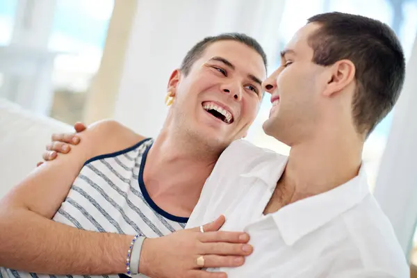 stock image Men, gay and happy couple in home relax with bonding connection or queer pride for homosexual, love or comfort. Male people, embrace and laughing joke in apartment for relationship, marriage or rest.