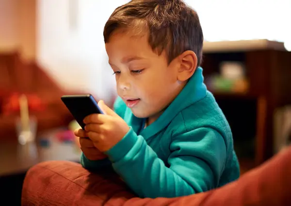 stock image Home, boy and kid with a smartphone, typing and playing online games with app and website information. Apartment, relax and child with a cellphone and mobile user with social media and communication.