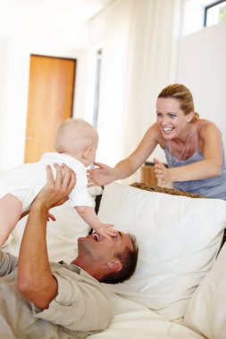 Komik, mutlu bir aile ve evdeki kanepede bebekle oynamak sevgi, ilgi ya da babanın annemle bağ kurması için. Baba, çocuk ve şirin bebek oturma odasında bağlanmak, gülümsemek ya da ebeveynler çocukla gülmek için..