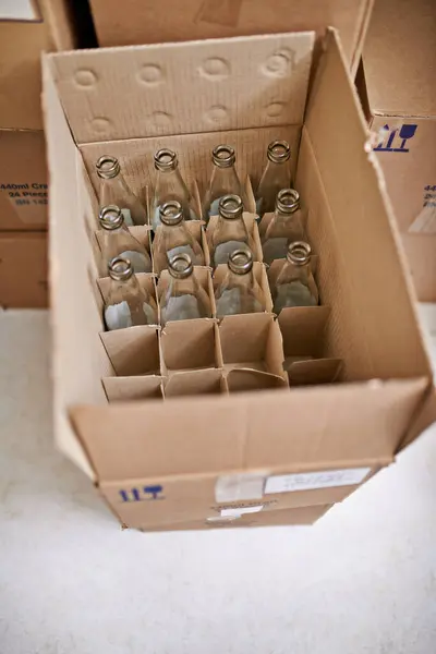 Empty beer bottle, box and storage in factory on floor, above and container for supply chain, process or delivery. Cardboard package, glass and brewery for alcohol, cider or production in warehouse.