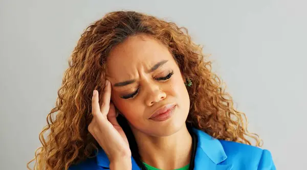 Frustrated woman, headache and stress with anxiety, mental health or depression on a gray studio background. Face of tired female person in fatigue, pressure or tension with overwhelmed emotion.