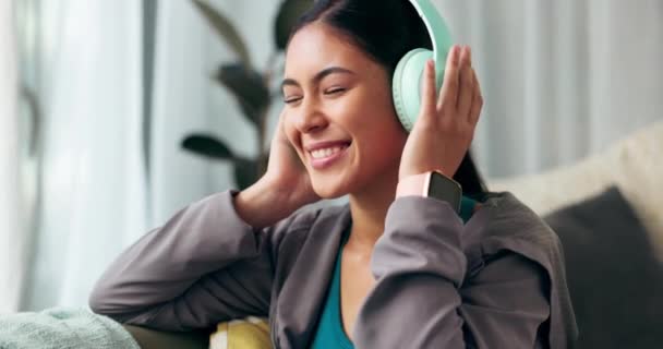 耳机和沙发为快乐的女人 听和收音机或歌曲流淌 在客厅里放科技 音频或电子音乐 让亚洲女性在沙发上放松身心 — 图库视频影像