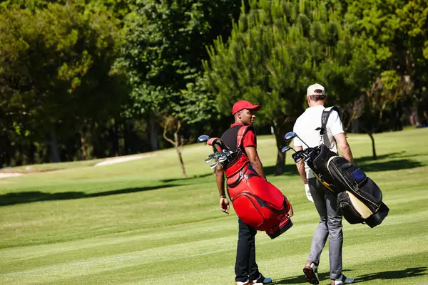 stock image People, walking and outdoor on course for golf, game and training at club in summer. Golfer, friends and men on grass turf in park together talking about practice of sport with healthy competition.