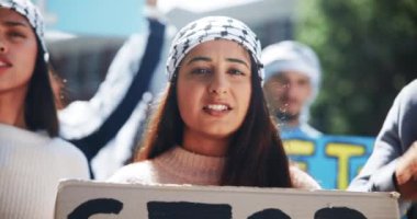 Protesto, savaş ve Filistin 'in desteğiyle adalet için soykırımı durdurmak için imzalı bir kadın. Öfke, konuşma ve özgürlük için bir grup insanla birlikte değişim için çatışmalara dikkat çekmek..