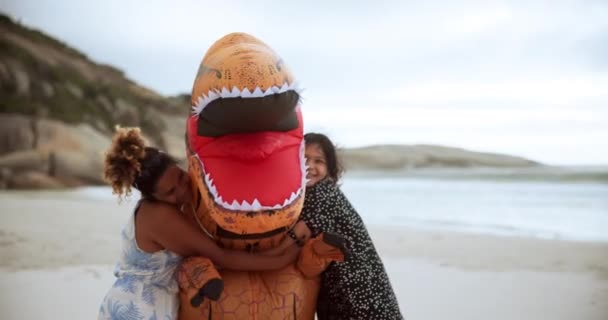 ビーチで恐竜の衣装を着たハッピー アウトドア 狂ったキャラクターとしてハグ トレックス 子供たちは休日や休暇に愛と世話で面白い膨脹可能なモンスターを受け入れます — ストック動画