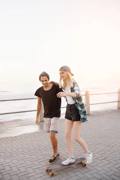 ボードウォークのカップル スケートボード アウトドア 幸せで 海で学び 遊ぶための手助け 女性とスケートのための教育 イタリアでの休暇のための遊歩道でのサポートと楽しい — ストック写真