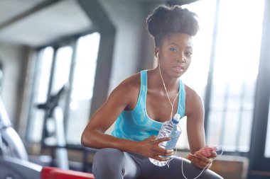 Telefon, kulaklık ve spor salonunda su, form uygulaması ya da internet aboneliği olan zenci kadın portresi. Sağlık, sağlık ve kız müzik listesini şişeyle, molayla ve spor kulübüyle birlikte akıllı telefondan kontrol ediyor..