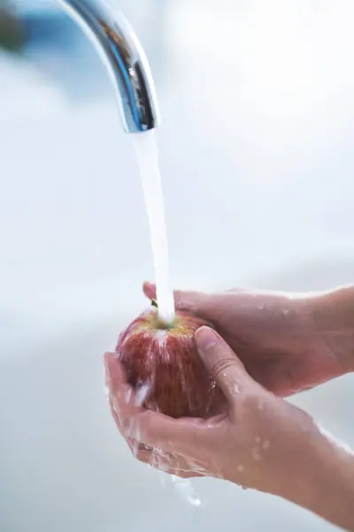 Water splash, hands and person cleaning apple, hygiene in kitchen with sustainability and disinfection, germs or bacteria. Health, wellness and nutrition with fruit, organic and fresh food at home.