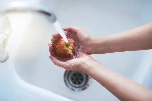 Water, hands and person cleaning apple, hygiene in kitchen with sustainability and disinfection, germs or bacteria. Health, wellness and nutrition with fruit, organic and top view of splash at home.