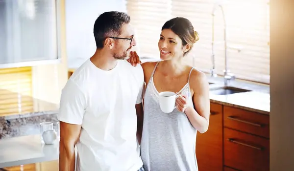 Love, coffee and couple hug in a kitchen for morning, conversation and bonding at home together. Marriage, trust and people embrace with tea in house for speaking, security and romance on weekend.