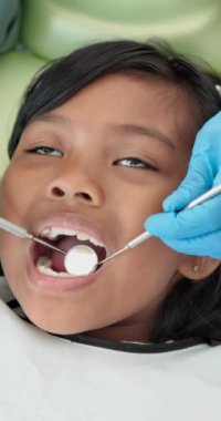 Diş hekimi, elleri ve aynalı bir kız hastanede diş, büyüme ve ağız sağlığını kontrol edecek. Çocuk, diş muayenesi ve diş eti hastalıklarına, diş çürüklerine veya klinikteki sağlığa yardımcı olacak aletler ağızda..