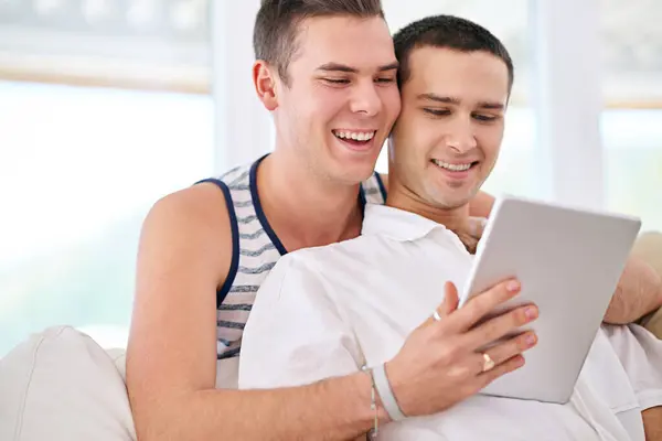 ビデオ グーグル用のソファーでタブレット ゲイのカップル サインアップまたは自宅でストリーミングサービス Lgbtq 愛と人々は デジタル アプリ Netflixでリビングルームで抱擁し 家で冷やします — ストック写真