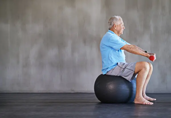 Senior man, dumbbells and exercise with ball for fitness, rehabilitation or physiotherapy at gym on mockup space. Elderly person, weightlifting or training for physical therapy, muscle or body health.